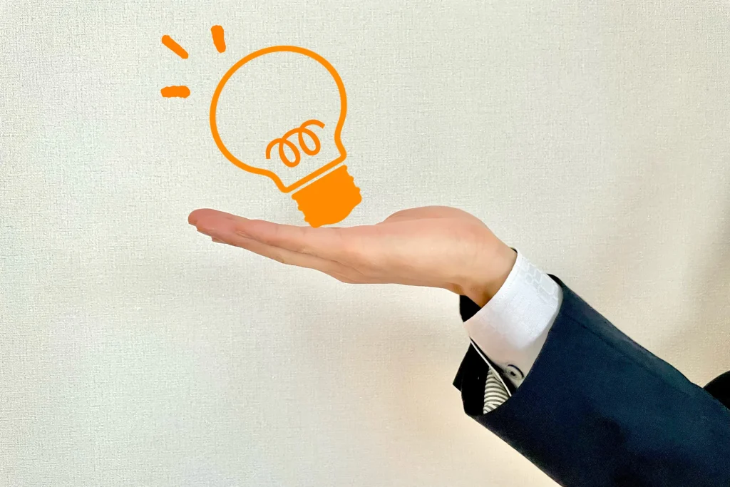 ビジネススーツを着用した手のひらに、オレンジ色の電球のアウトラインが描かれた画像