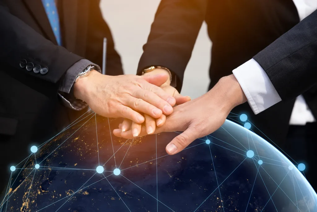 ビジネスパーソンが手を重ねて協力する様子と地球のネットワークイメージ