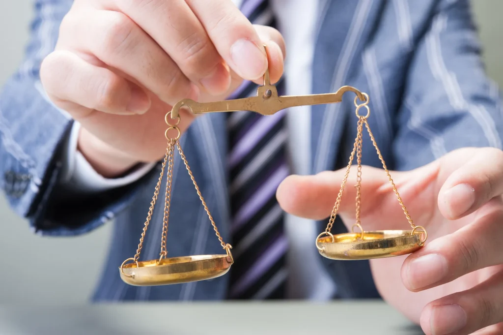 スーツを着たビジネスマンが、公平性やバランスを象徴する金色の天秤を手に持っている様子