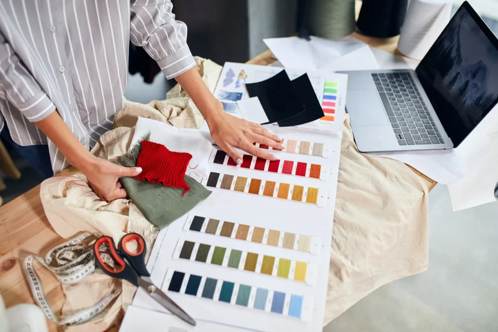 デスクの上で生地サンプルやカラーチャートを確認しながら、服のデザインを検討するデザイナーの手元