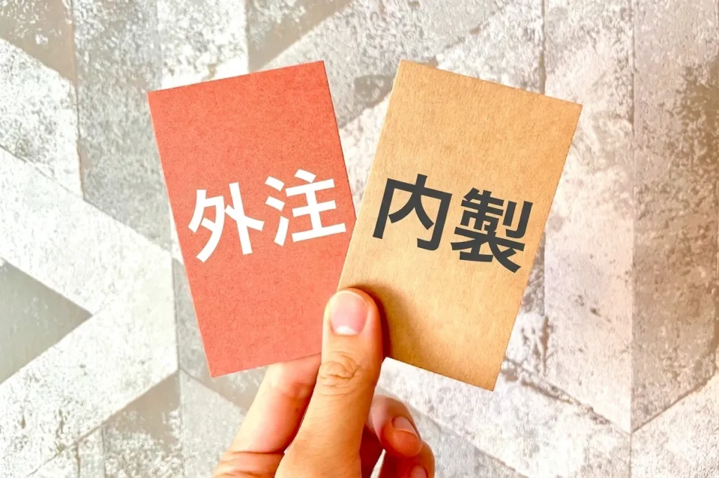 「外注」と「内製」と書かれた2枚のカードを提示して比較検討する様子