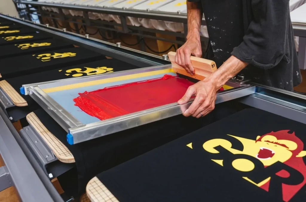 シルクスクリーン印刷で黒いTシャツに赤いインクを刷る様子