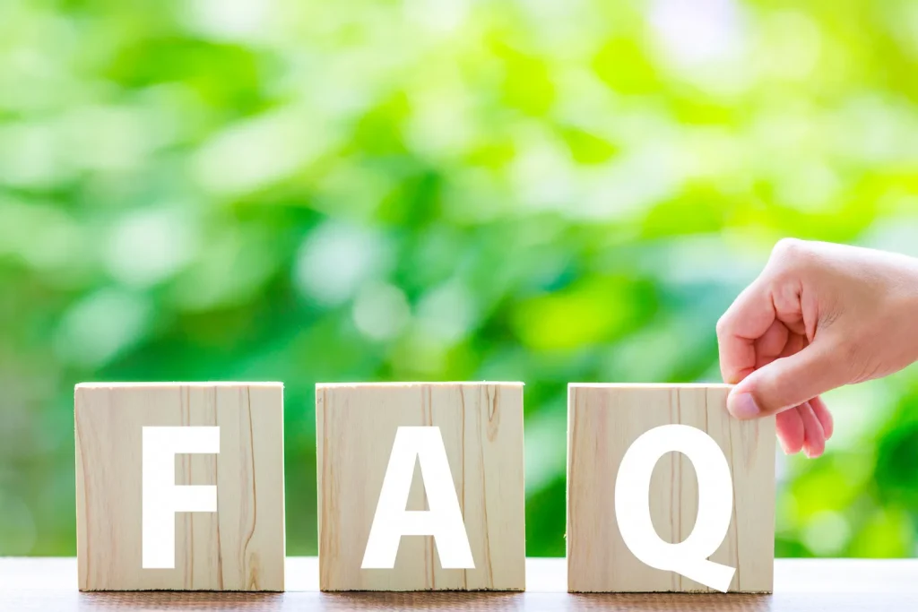 緑の背景をバックに「FAQ」と書かれた木製ブロックを並べる手