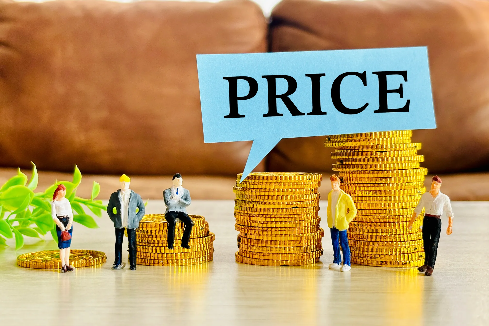 積み上げられた金貨の横に立つミニチュアの人々と、「PRICE」と書かれた吹き出しの画像