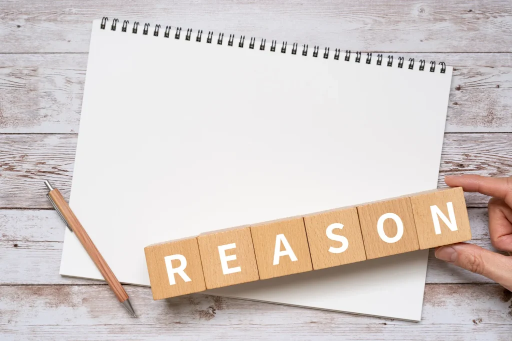 白いノートの上にREASONと書かれた木製ブロックを置く様子