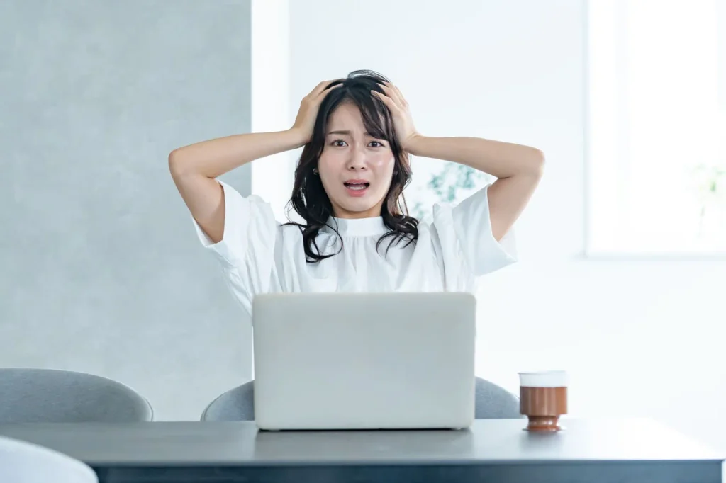 パソコンの前で頭を抱えて困った表情をする女性